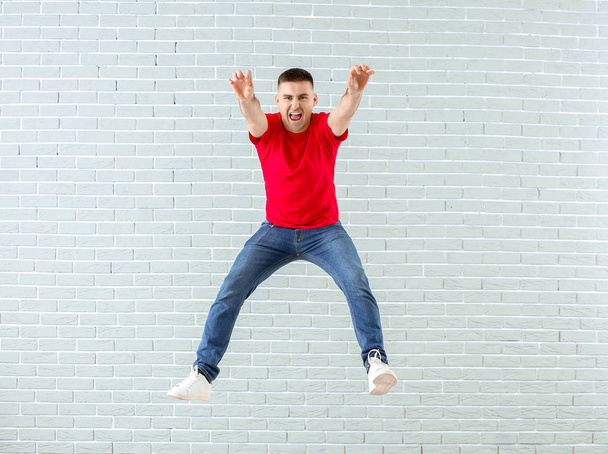 Jumping young man against brick wall - Фото, зображення