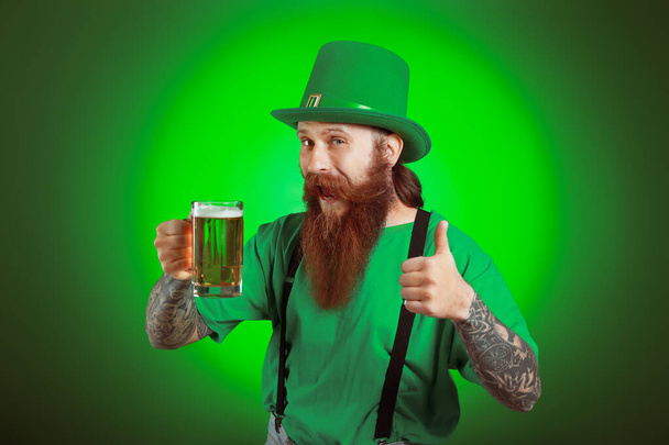 Bearded man with glass of beer showing thumb-up gesture on dark background. St. Patrick's Day celebration - Photo, image