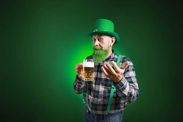 Funny mature man with glass of beer inviting viewer on dark background. St. Patrick's Day celebration - Foto, Imagen