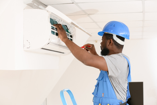 Afrikanisch-amerikanischer Elektriker repariert Klimaanlage in Innenräumen - Foto, Bild