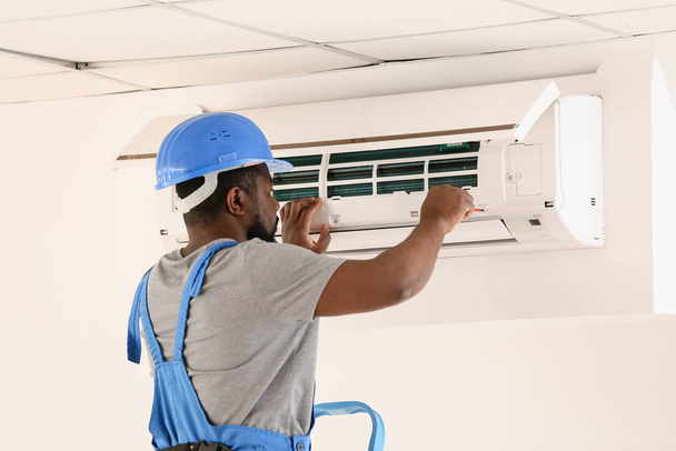 アフリカ系アメリカ人の電気技師は屋内でエアコンを修理する - 写真・画像