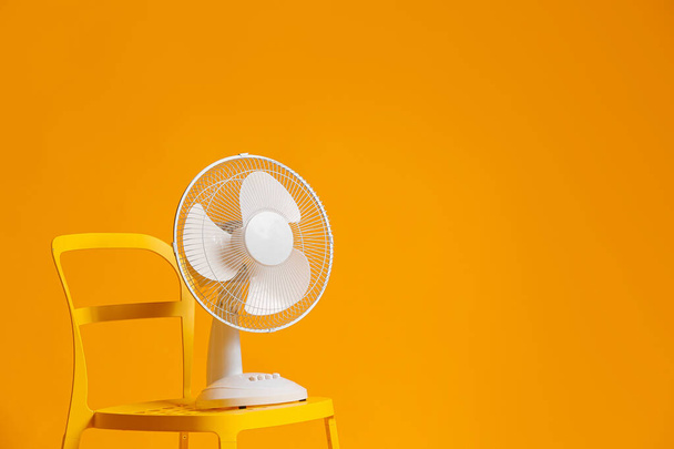 Electric fan on chair against color background - 写真・画像