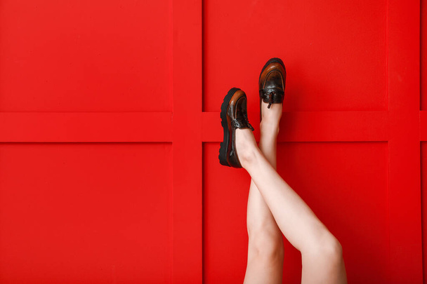 Legs of young woman in stylish shoes against color background - 写真・画像