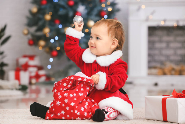 Leuke kleine baby in kerstman kostuum en met kerstcadeaus thuis - Foto, afbeelding