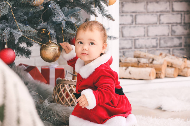 Cute little baby w stroju Świętego Mikołaja w pobliżu choinki w domu - Zdjęcie, obraz