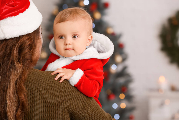 Young mother with cute little baby in Santa Claus costume on Christmas eve at home - Φωτογραφία, εικόνα