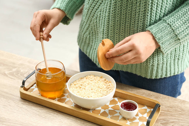 Woman adding honey to oatmeal at wooden table indoors, closeup - Valokuva, kuva