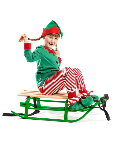 Little girl in costume of elf sitting on sledge against white background - Photo, image