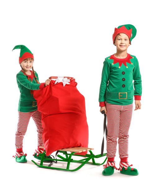Petits enfants en costume d'elfe et avec sac Père Noël sur luge sur fond blanc
 - Photo, image