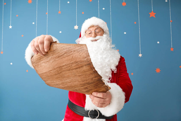 Santa Claus reading wish list on color background - Foto, Imagen