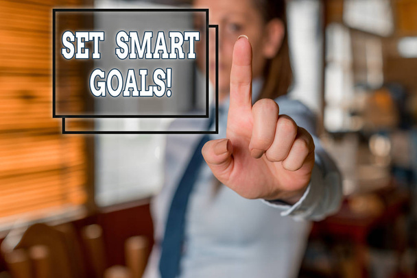 Pisząc notatkę pokazującą Set Smart Goals. Lista pokazów zdjęć biznesowych, aby wyjaśnić swoje pomysły skupić wysiłki wykorzystać czas mądrze zamazana kobieta w tle wskazując palcem w pustej przestrzeni. - Zdjęcie, obraz