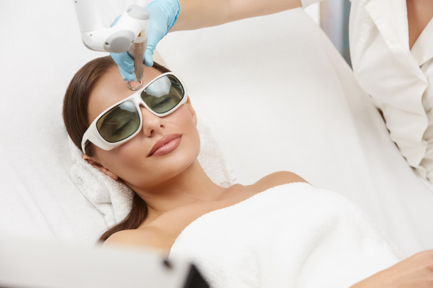 relaxed woman receiving laser procedures in beauty salon on white bed, female getting facial treatment in luxury spa - Photo, Image