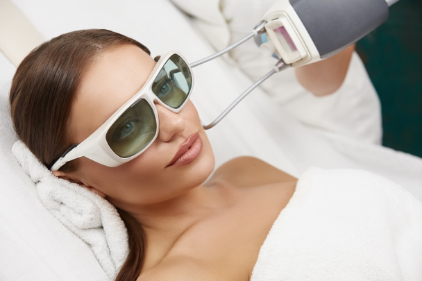 beautiful woman wearing protection glasses lying in white spa salon and receiving laser rejuvenation, amazing girl having facial care - Φωτογραφία, εικόνα