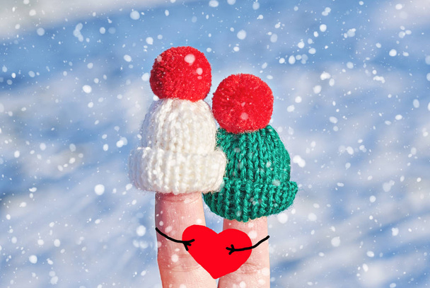 Divertidos dedos de pareja en sombreros de lana de punto con grandes corazones rojos en las manos
 - Foto, imagen