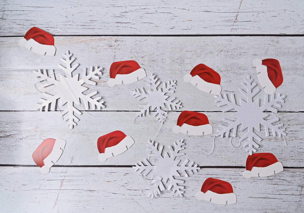 Santa 's papieren hoeden en papieren sneeuwvlokken op houten ondergrond, - Foto, afbeelding