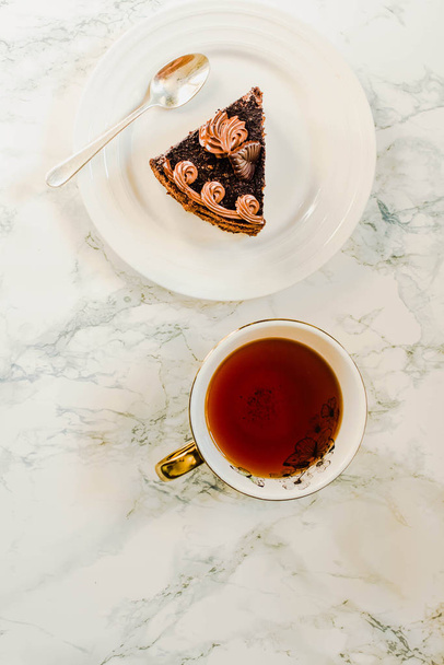 Plate with slice of homemade chocolate cake and yellow gold cup  - Fotó, kép