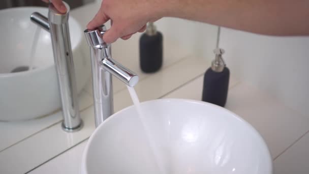 Badezimmer. Waschbecken und Wasserhahn in Großaufnahme. männliche Hand öffnet und schließt das Wasser. 4k - Filmmaterial, Video