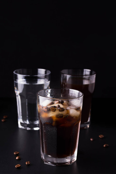 コーヒー豆や食材の隣に黒い背景のアイスコーヒー - 写真・画像