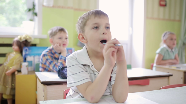 Çocuk ağzında bir kalemle düşünerek bir kalem tutuyor. - Video, Çekim