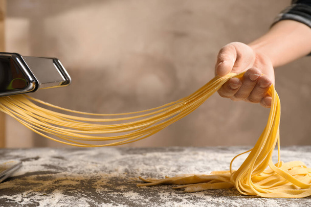 Woman preparing noodles with pasta maker machine at table, close - Foto, Bild