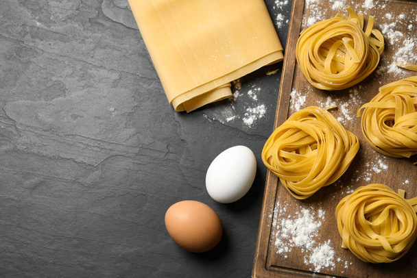 Raw tagliatelle pasta and products on black table, flat lay - Foto, Imagen