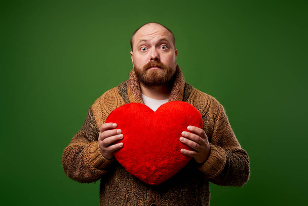 Man holding toy heart while standing on empty green background - Fotó, kép