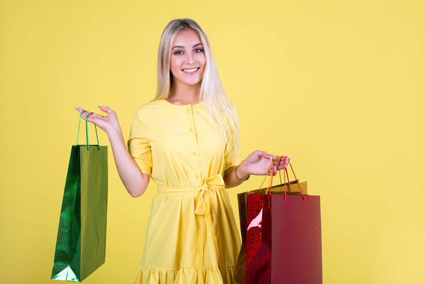 beautiful young woman in a dress on a yellow background with packages in hands - Фото, зображення