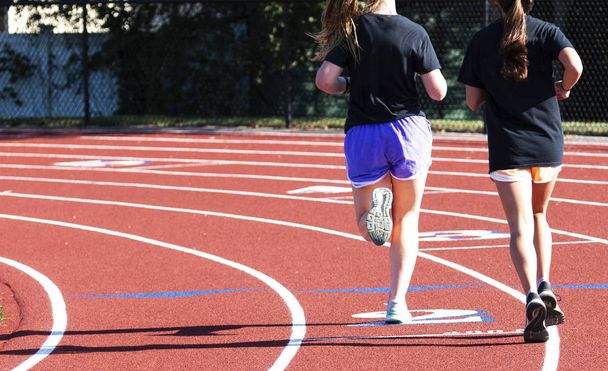 Dos chicas de secundaria corriendo en la curva en una pista
 - Foto, Imagen