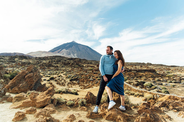 Beautiful young couple of lovers posing on a rocky field on a background of a volcano - Фото, зображення