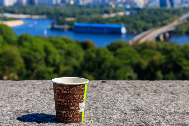 Coupe de café en papier sur un parapet en pierre surplombant le paysage urbain de Kiev, Ukraine - Photo, image