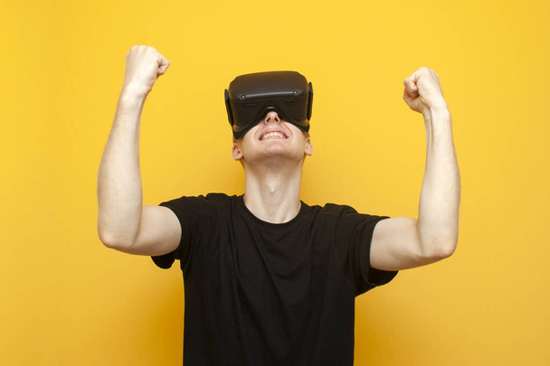 эмоциональный парень в очках VR выигрывает виртуальную игру, геймер радуется победе над желтым фоном
 - Фото, изображение