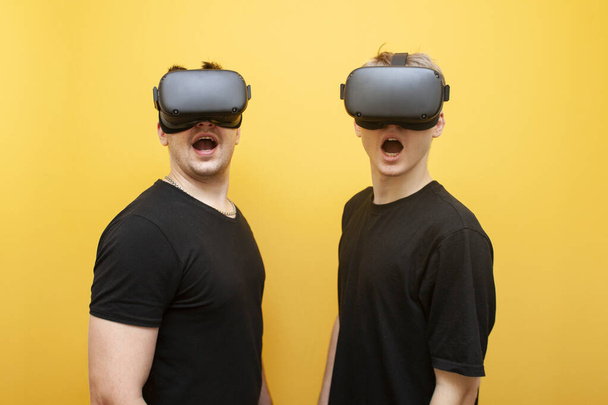 twee verraste jongens in Vr bril op een gele achtergrond, een paar vrienden van gamers in virtual reality bril - Foto, afbeelding