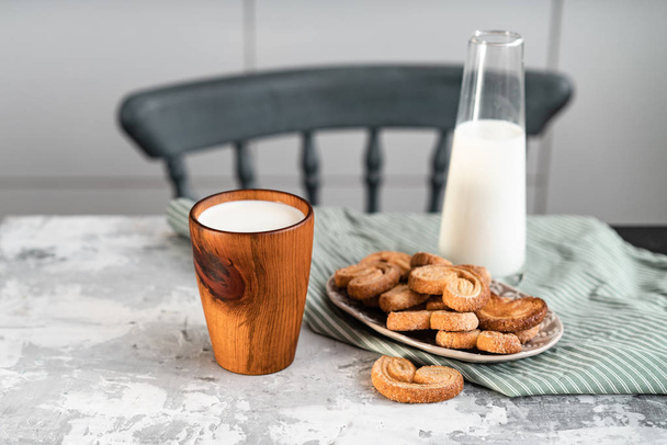 A wooden glass with milk on the kitchen table near to cookies - Φωτογραφία, εικόνα