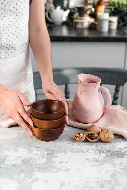 Woman's hands in an apron put on the kitchen table with a jug a stack of wooden plates - Foto, imagen