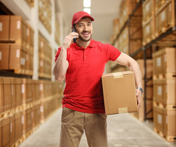 Delivery man holding a package and talking on the phone in a sto - Foto, imagen