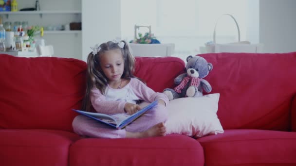 Χαριτωμένο μικρό παιδί είναι stting στον καναπέ με την ανάγνωση ενός βιβλίου - Πλάνα, βίντεο