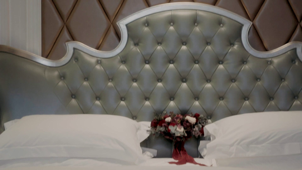 σε ένα μεγάλο όμορφο κρεβάτι γλείφει ένα κόκκινο μπουκέτο λουλούδια - Πλάνα, βίντεο