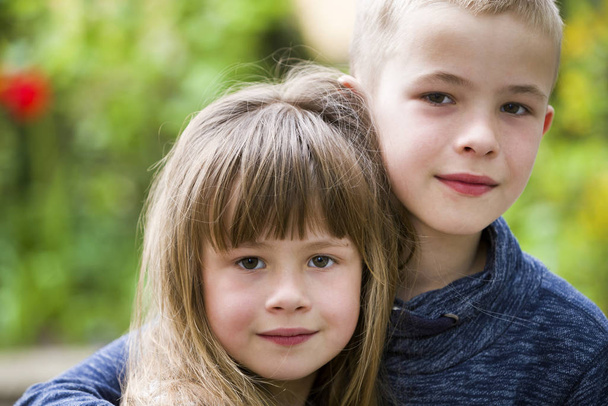 Dva roztomilé světlovlasé děti sourozenci, mladý chlapec bratr objímající sestru dívku venku na jasně zeleném pozadí bokeh. Rodinný vztah, přátelství a koncept lásky. - Fotografie, Obrázek