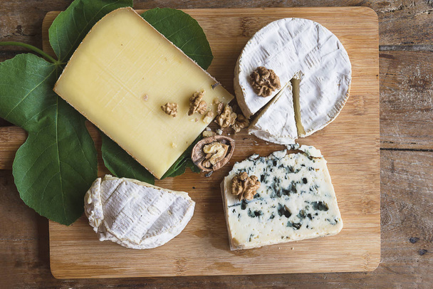 Divers fromages français, noix, feuille de figuier sur la planche à découper en bois
 - Photo, image