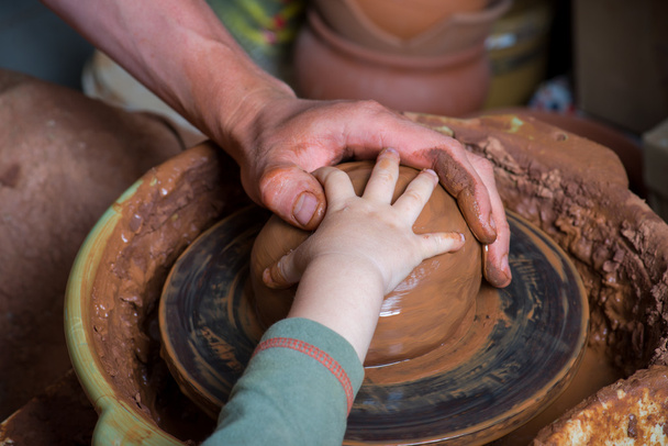 ein Töpfer gibt dem Schüler die Hand, um ihm bei der Arbeit mit der Keramikscheibe zu helfen - Foto, Bild