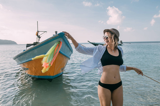 Jonge vrouw op een tropisch strand bij een vissersboot - Foto, afbeelding