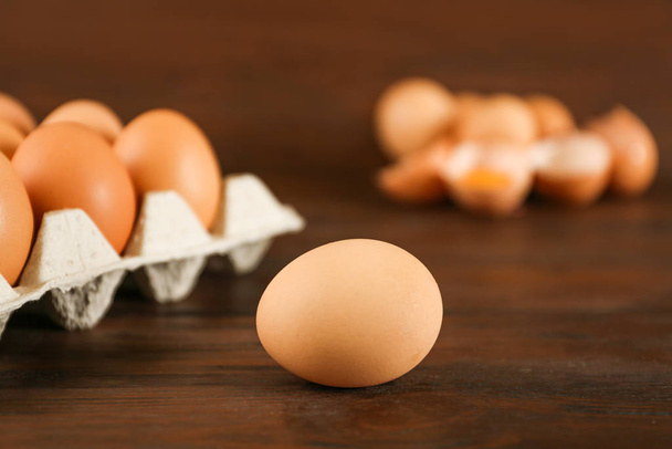 Raw chicken egg near carton tray on wooden table - Zdjęcie, obraz