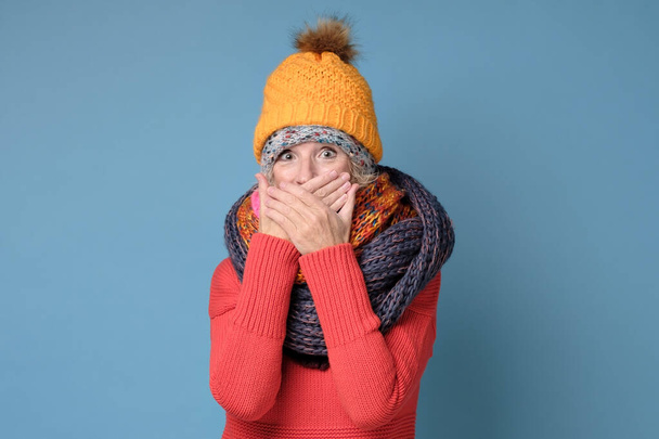 Γυναίκα με χειμωνιάτικα ρούχα έχει εκπληκτική έκφραση, που καλύπτει το στόμα με τα χέρια - Φωτογραφία, εικόνα