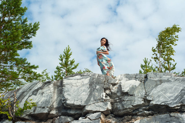 Mermer kayalıklarda poz veren uzun elbiseli genç kadın. - Fotoğraf, Görsel