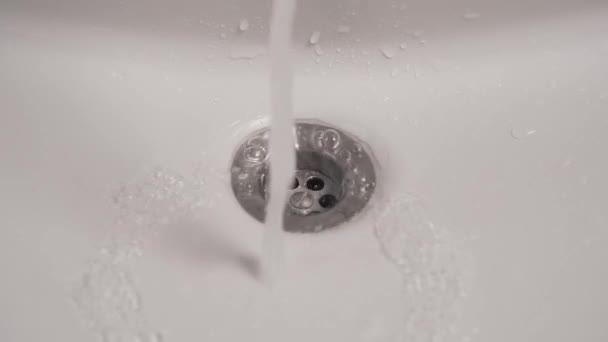 Water drips and then flows in a white sink, flowing into a hole with a stainless shiny lattice. Slow motion close up. The concept of saving tap water and leaks - Footage, Video