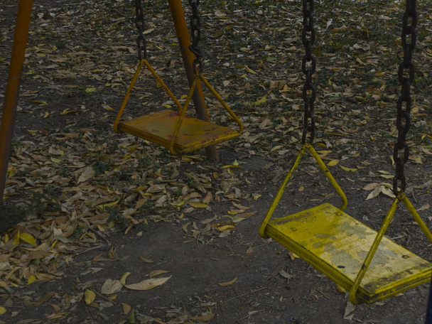 Columpios viejos en parque solitario, con oxido en color amarillo y naranja que están daados y temen. - Foto, Imagen