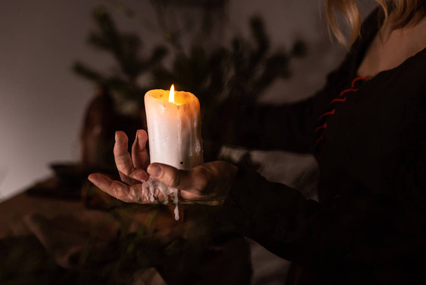 A woman dressed in a medieval dress holds a burning white candle in her hand. Mystery witch - Foto, Imagen