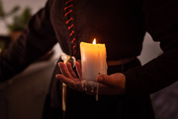 A woman dressed in a medieval dress holds a burning white candle in her hand. Mystery witch - Foto, Imagen