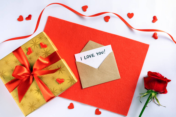 Caja de regalo de oro con cinta roja en tela, sobre, tarjeta con iscripción te amo y pequeños corazones
 - Foto, Imagen