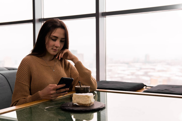 νεαρή γυναίκα καλεί έναν αριθμό στο τηλέφωνο, ενώ κάθεται σε ένα καφέ - Φωτογραφία, εικόνα